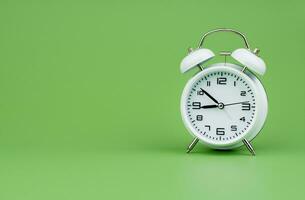 White alarm clock tells time working with time importance of time punctuality White clock on a green background photo