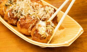 cerca arriba de takoyaki o pulpo pelotas en palillos. japonés comida en de madera antecedentes. foto