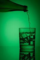 beautiful bottle with water and glass with ice and water on a green background photo