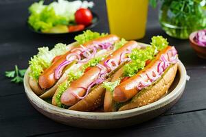 Hot dog with  sausage, pickled cucumber, tomatoes, red onions and lettuce on dark wooden background. Summer hotdog. photo