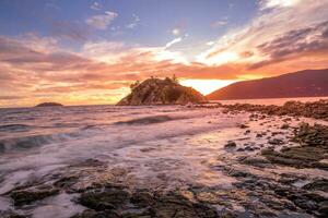 un hermosa puesta de sol terminado el Oceano con rocas y un pequeño isla foto