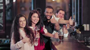 gruppo di ragazze e ragazzi a il bar con un' birra sorridente e mostrando pollice su video