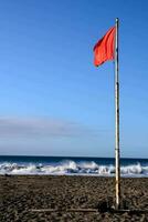 un rojo bandera en el playa con olas en el antecedentes foto