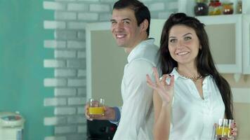 Couple standing back to back holding orange juice, the girl shows OK video