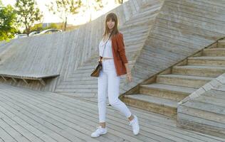 Happy   stylish female student posing in modern park , wesring white jeans, jacket and t-shirt.  Full lenght. photo