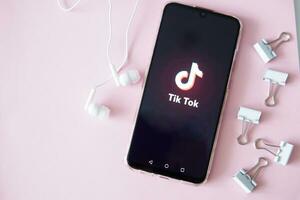 ver, rusia-abril 9, 2020, el tik tok logo en el teléfono inteligente pantalla en rosado antecedentes con auriculares. tic-tac icono. logo de el Actual aplicación Tik Tok social red. foto