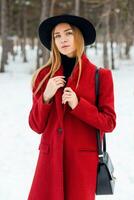 Outdoor fashion portrait of glamour l young  cheerful  stylish lady wearing trendy  winter  outfit , black wool  hat  and red coat . Cold season.Blonde long hair. Full lips, blue eyes. photo