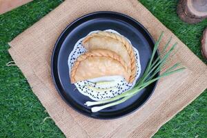 Curry puff or Pastel Goreng is Pastry Popular in Indonesia.fried pastry with filling of sauted vegetable , chicken and boiled egg. accompanied with  sauce or raw chilli pepper photo