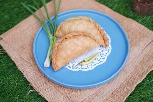 Curry puff or Pastel Goreng is Pastry Popular in Indonesia.fried pastry with filling of sauted vegetable , chicken and boiled egg. accompanied with  sauce or raw chilli pepper photo