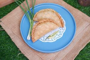 Curry puff or Pastel Goreng is Pastry Popular in Indonesia.fried pastry with filling of sauted vegetable , chicken and boiled egg. accompanied with  sauce or raw chilli pepper photo