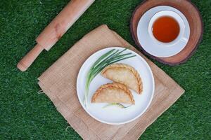Curry puff or Pastel Goreng is Pastry Popular in Indonesia. fried pastry with filling of sauted vegetable, chicken and boiled egg. accompanied with  sauce or raw chilli pepper photo