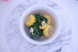 Sayur Bening Daun kelor jagung or Moringa Oleifera clear soup with sweet corn served in bowl photo