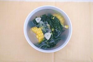 Sayur Bening Daun kelor jagung or Moringa Oleifera clear soup with sweet corn served in bowl photo