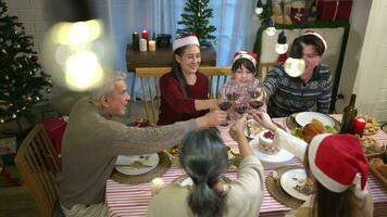 feliz ásia família a comemorar Natal juntos às lar. alegre Senior pais e crianças dentro santa chapéu tilintar óculos do vermelho vinho. video