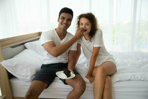 Smiling and happy couple having dessert in bed in the morning photo