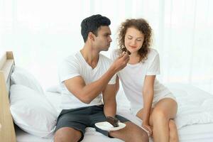 Smiling and happy couple having dessert in bed in the morning photo