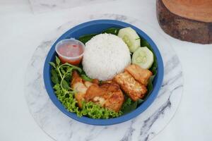 Ayam penyet a East Javanese cuisine smashed fried chicken dish with floss sambal slices of cucumbers fried tofu and tempeh photo