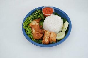 Ayam penyet a East Javanese cuisine smashed fried chicken dish with floss sambal slices of cucumbers fried tofu and tempeh photo