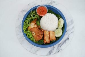 Ayam penyet a East Javanese cuisine smashed fried chicken dish with floss sambal slices of cucumbers fried tofu and tempeh photo