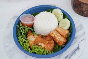 Ayam penyet a East Javanese cuisine smashed fried chicken dish with floss sambal slices of cucumbers fried tofu and tempeh photo