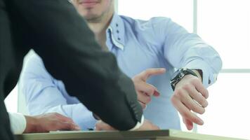 Serious businessman sitting at the negotiating table in the office and indicates your watch video