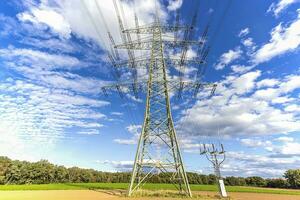 Image of an electricity pylon from the ground perspective in front of a blue sky with white clouds photo
