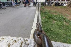 Picture along an iron chain that acts as a partition between the footpath and a green area photo