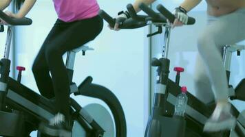 Two young ladies girl pedaling on the simulator look at each other and smiling video