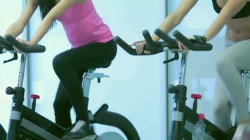 Two young ladies girl pedaling on the simulator and looking at the camera video