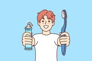 Little boy holds toothpaste and toothbrush showing snow-white smile and recommending brushing teeth regularly. Child independently monitors health of own teeth in order to get rid of caries vector