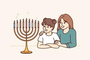 preadolescente muchachas hermanas Mira a Menorah con ardiente velas y alegrarse a Acercarse de fiesta de Jánuca Menorah en mesa cerca dos contento niños simboliza judío religión y honrando tradiciones vector