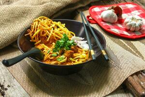 Noodles with pork and vegetables in a bowl on the table, Khao Soi Kai, Northern Style Curried Noodle Soup with choice of pickled chicken photo