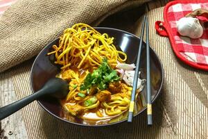 Noodles with pork and vegetables in a bowl on the table, Khao Soi Kai, Northern Style Curried Noodle Soup with choice of pickled chicken photo