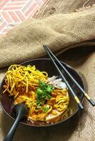 Noodles with pork and vegetables in a bowl on the table, Khao Soi Kai, Northern Style Curried Noodle Soup with choice of pickled chicken photo