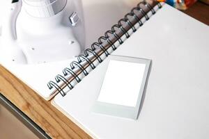 an open notebook is a white sheet, there is an instant print camera and an instant print photo next to it