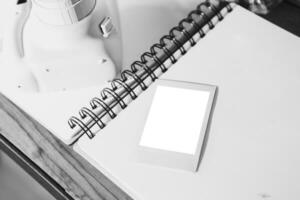 an open notebook is a white sheet, there is an instant print camera and an instant print photo next to it