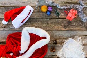 Santa Claus suit, small tree, pinecone, Christmas balls, garland, gift on wooden background. Top view. Toned image. photo