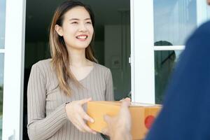 Happy smiling woman receives boxes parcel from courier in front house. Delivery man send deliver express. online shopping, paper containers, takeaway, postman, delivery service, packages photo