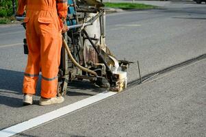 Worker wearing uniform is making the white line on road with painting machine photo