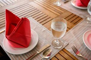 comida de madera mesa conjunto con cerámico vajilla, plata utensilio, rojo servilleta y agua foto
