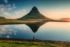 Volcanic Kirkjufell mountain with lake reflection and traveler man standing during sunrise at Iceland photo