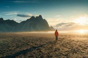 Sunrise over Vestrahorn mountain with a tourist man walking on black sand beach in summer photo