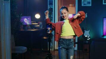 Kid doing viral dance choreography in living room with 3D rendered animations on computer screens in background. Child dancing in neon lit home studio interior, producing content with cellphone video