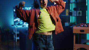 Tilt up shot of excited girl doing captivating dance moves for social network platforms, doing viral challenge. Smiling kid having fun recording video for online fans in dimly lit home studio