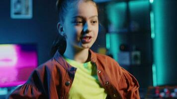 Close up shot of smiling kid dancing in dimly lit home studio interior, producing content for online channel. Excited child doing viral dance choreography in apartment illuminated by neon lights video