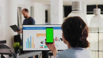 Employee uses phone app with greenscreen sitting at desk in creative agency office, analyzing isolated display that runs copyspace template. Woman works with smartphone layout. Handheld shot. video