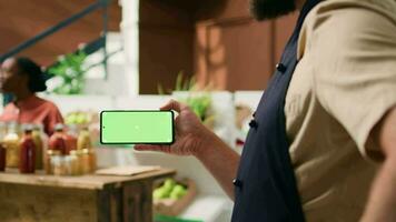 lokal Verkäufer hält grüner Bildschirm Telefon mit isoliert Anzeige, präsentieren Copyspace Technologie auf Handy, Mobiltelefon Telefon. Person suchen beim leer Chromakey Bildschirm beim Lebensmittelgeschäft Geschäft registrieren. video