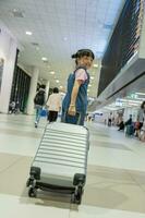 linda contento niño niña con maleta a aeropuerto Terminal. niño y familia de viaje vacaciones para esperando embarque en Terminal. familia viaje concepto. foto