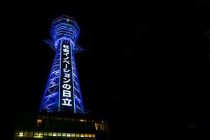 Osaka City, JP, 2019 - Tsutenkaku tower with blue neon lights and Japanese lettering on night time background. Tsutenkaku is a tower and one landmark of Osaka, Total height is 103 m. photo