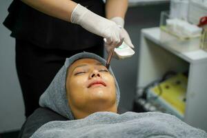 Closeup cosmetologist use cosmetic brush applying facial jelly's gel on woman client face in beauty clinic. photo